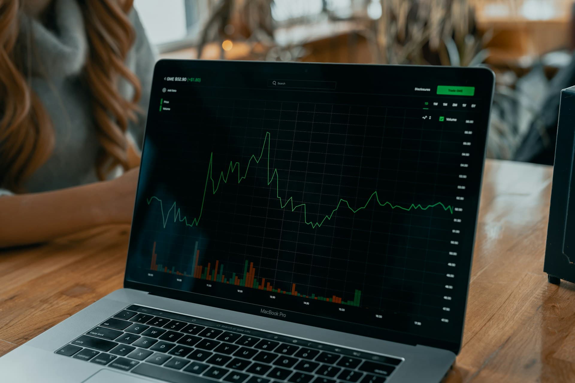 A laptop on a wooden table showing an intraday price chart with volume bars beneath it