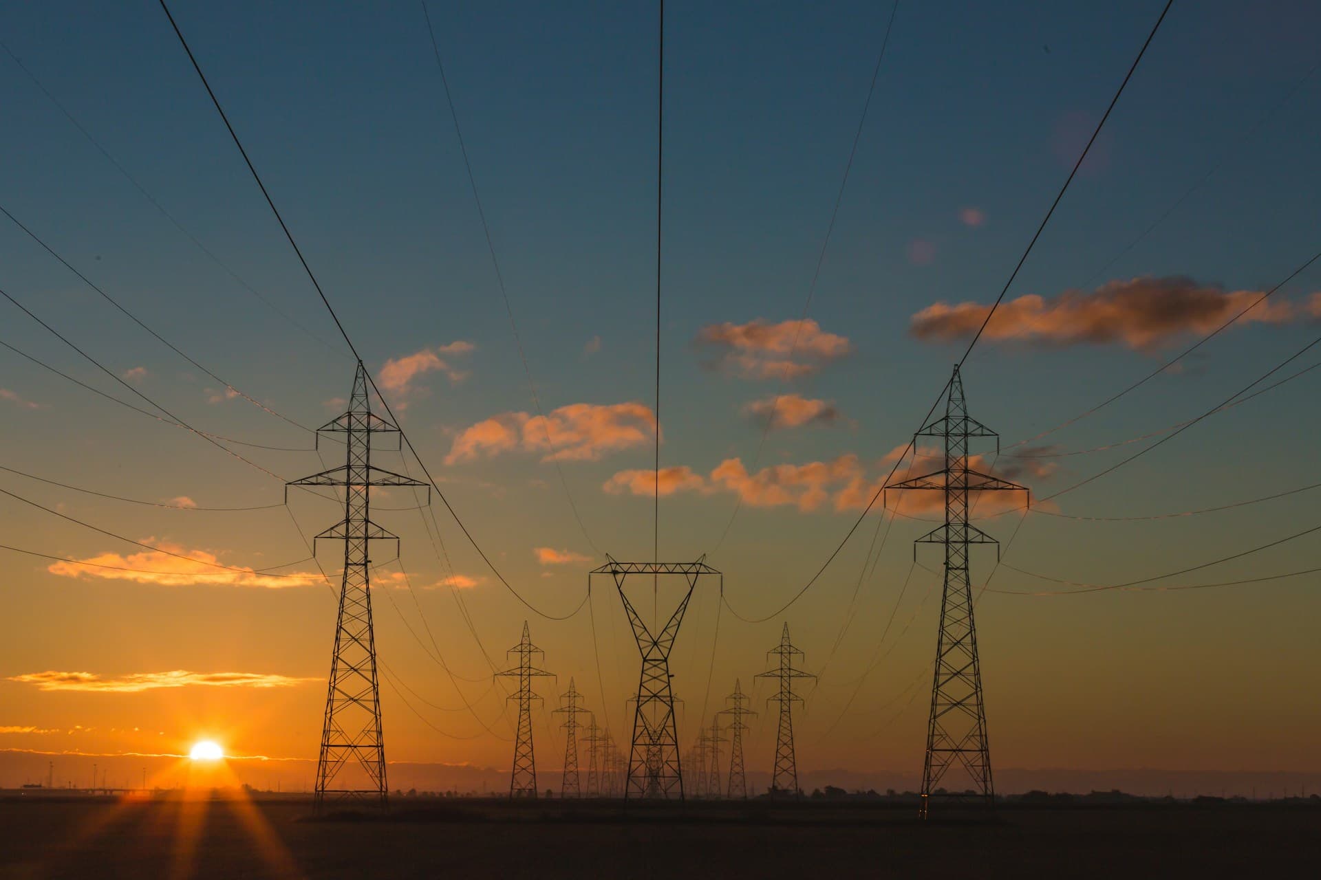 Electricity pylons and power lines silhouetted against an orange sunset